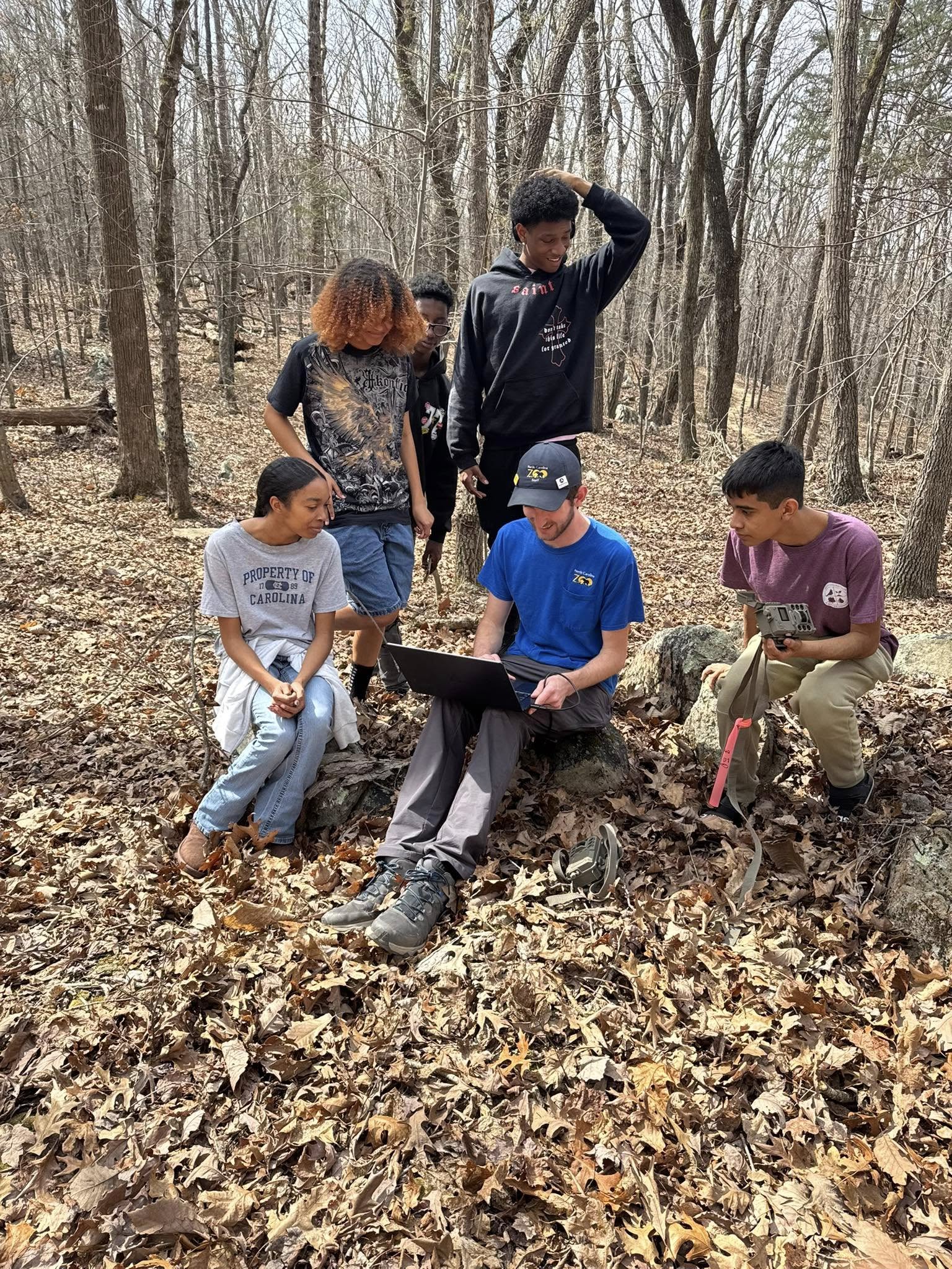 Students and expert holding a laptop sitting and standing outside in leaves