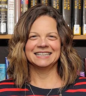 Dr. Kristin Robins smiling for a photo in front of a bookshelf filled with books