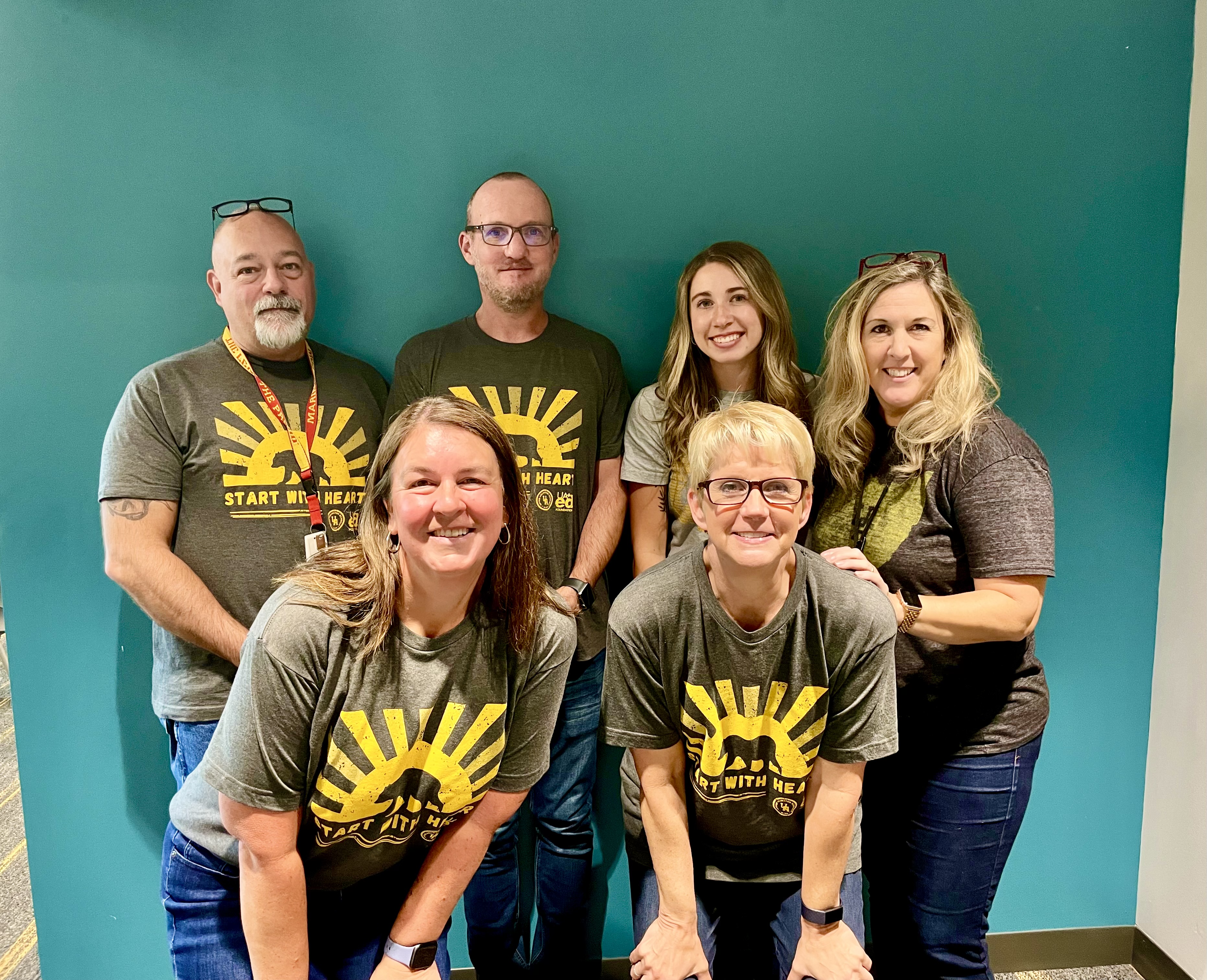 The six Upper Arlington High School counselors posing for a photo in gray shirts in front of a bluish-green background