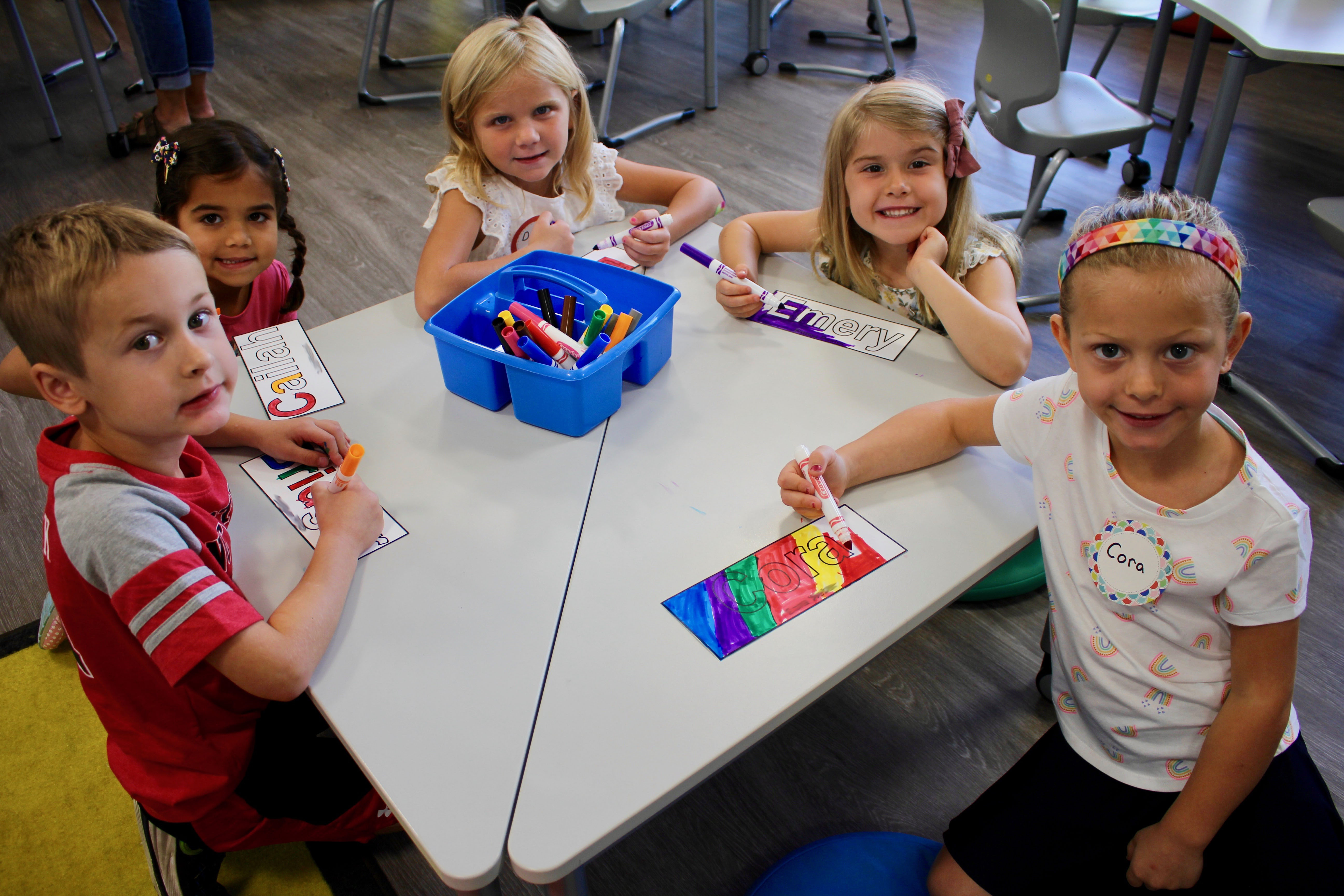 Five kindergarteners sitting at a table coloring their nametags