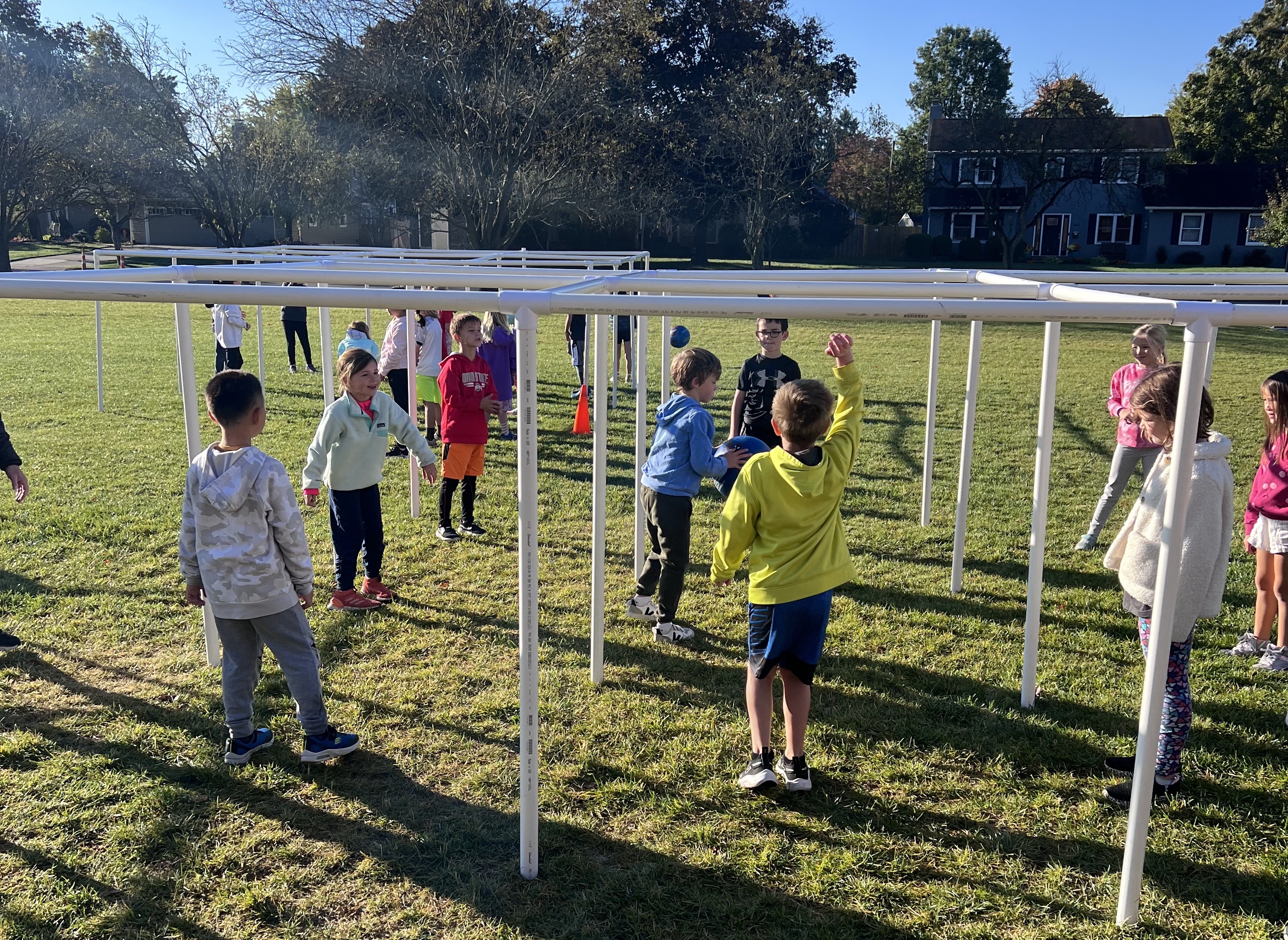 Students engaging in a 9-square activity involving a structure made of PVC pipes